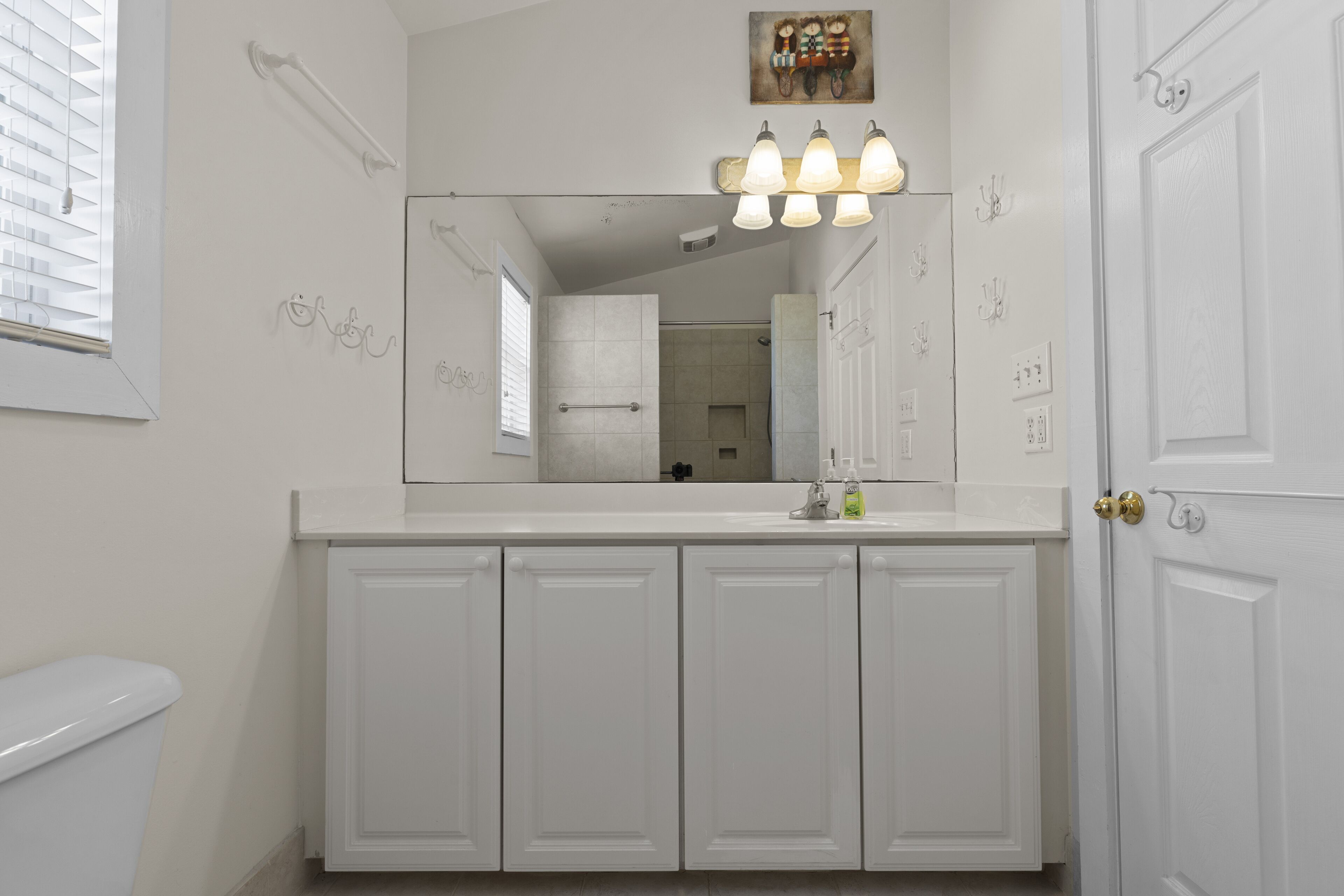 Un bagno con un mobile lavabo bianco, uno specchio grande e un lampadario sopra lo specchio.
