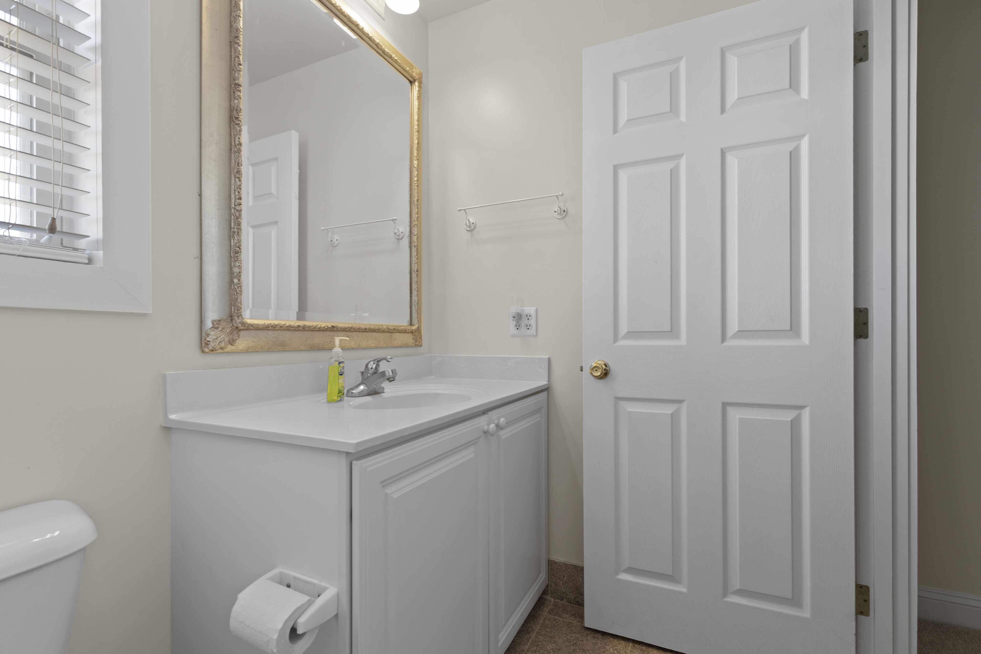 Une salle de bain avec un lavabo blanc, un miroir avec un cadre doré et une porte blanche.