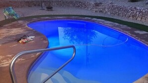Ein Schwimmbecken mit Metallleiter, umgeben von einer Steinmauer und einer Rasenfläche.