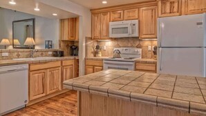 Une cuisine moderne avec des meubles en bois, un four à micro-ondes, un réfrigérateur et un îlot central recouvert de carreaux.
