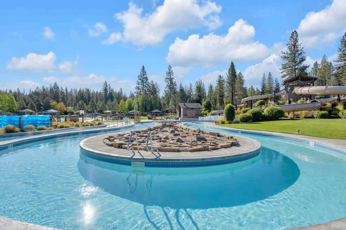 A large outdoor swimming pool with a circular hot tub in the center, surrounded by lounge chairs and a wooden deck.
