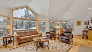A spacious living room with a large window, a leather sofa, a wooden coffee table, and a fireplace. - AC, pet friendly, inside Sunriver, EV charger (Sunriver)