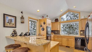 A modern kitchen with wooden cabinets, granite countertops, and a large island with stools. - AC, pet friendly, inside Sunriver, EV charger (Sunriver)