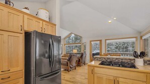 A modern kitchen with wooden cabinets, a black refrigerator, a gas stove, and large windows offering a view of snow-covered trees. - AC, pet friendly, inside Sunriver, EV charger (Sunriver)