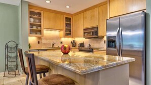 Una cocina moderna con armarios de madera, un refrigerador de acero inoxidable, un microondas y una encimera de granito.