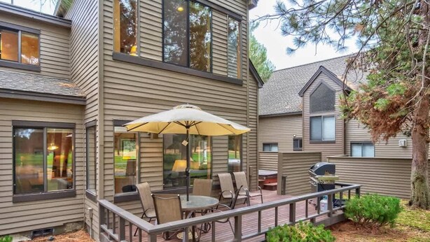 Una casa de dos pisos con un patio cubierto que cuenta con muebles para exteriores y una parrilla.
