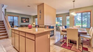 Una cocina amplia con una isla central, un comedor con mesa y sillas, y una escalera que lleva a otro nivel.