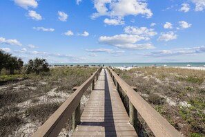 A wooden boardwalk leading to a beach with a clear sky and distant ocean view.