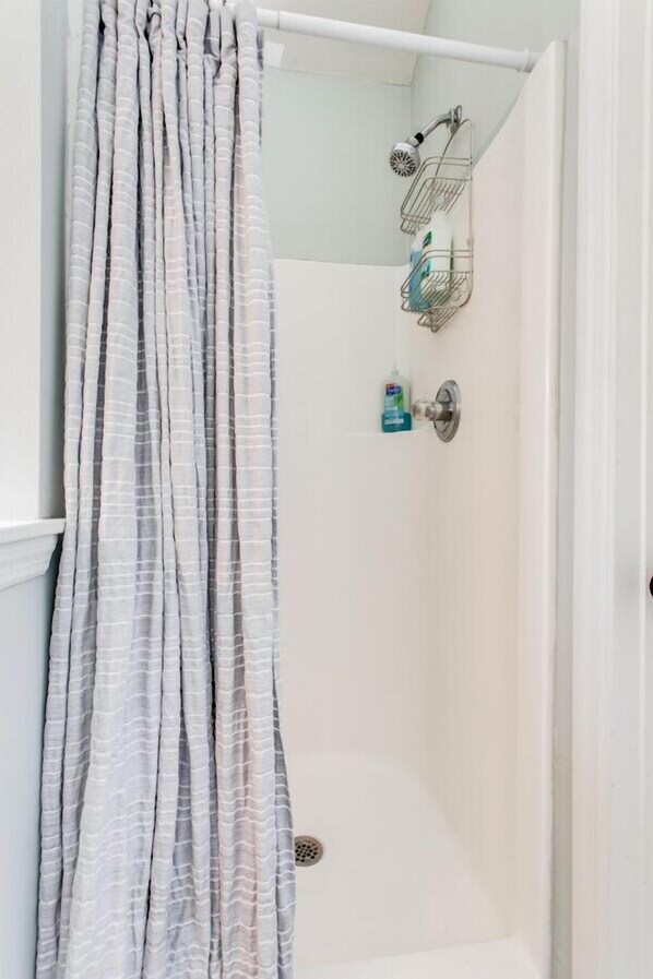 Ein Badezimmer mit Dusche, Vorhang und Ablage für Toilettenartikel.