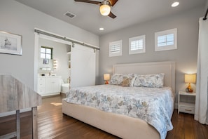 A bedroom with a large bed, a ceiling fan, and a view of the bathroom.