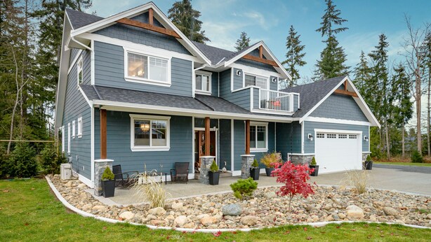 A two-story house with a front porch, a garage, and a landscaped front yard with rocks and plants.