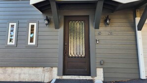 A house with a dark brown front door, a small porch, and a number '211' displayed on the wall.