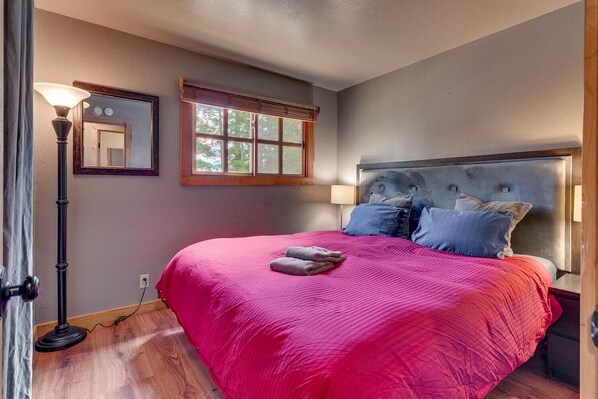 A bedroom with a large bed, a nightstand, a lamp, and a window with blinds.