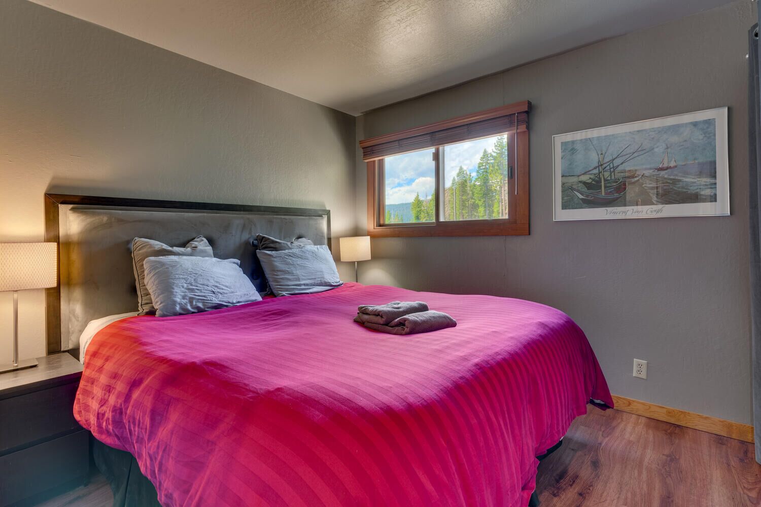 A hotel room with a large bed, a window with a view of trees, and a painting on the wall.