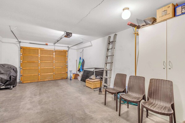 A garage with a wooden door, a ladder, wicker chairs, and a ceiling light fixture.