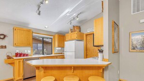 Eine moderne Küche mit Holzsäcken, einer großen Kochinsel mit Barhocker, einem Geschirrspüler und einem Kühlschrank.