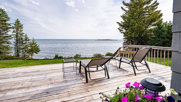 Une terrasse en bois avec deux chaises et une table, d’où l’on peut admirer un plan d’eau et une étendue de terre au loin.