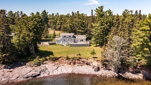 Une maison à deux étages avec une grande pelouse devant et un étang au premier plan.