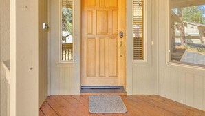 Una porta d'ingresso in legno con una maniglia di metallo, un piccolo gradino che conduce alla porta e un tappetino grigio sul portico in legno.
