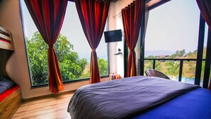 A bedroom with a large bed, a TV, and a view of greenery and mountains. - The Bob house (Mawal)