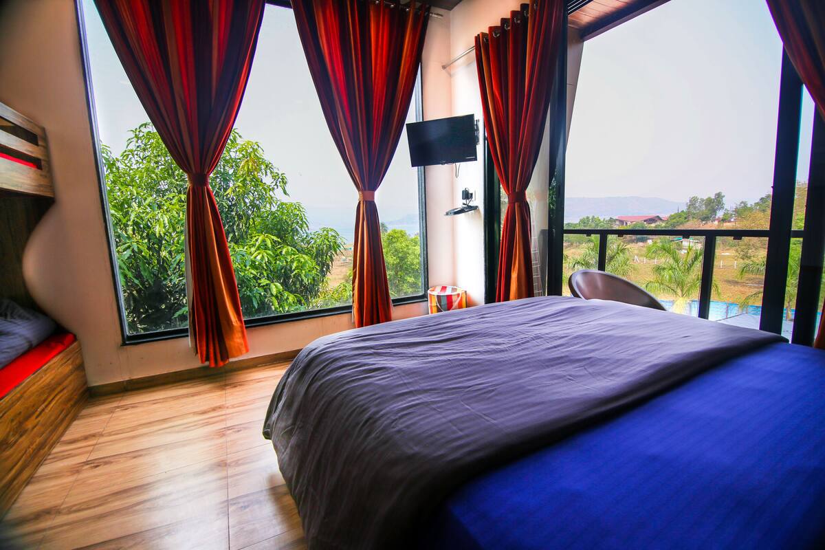 A bedroom with a large bed, a TV, and a view of greenery and mountains.