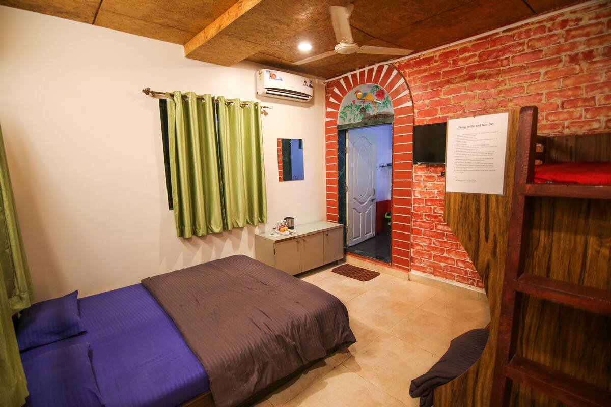 A room with a bed, a desk, a red brick wall, a ceiling fan, and a door with a sign.