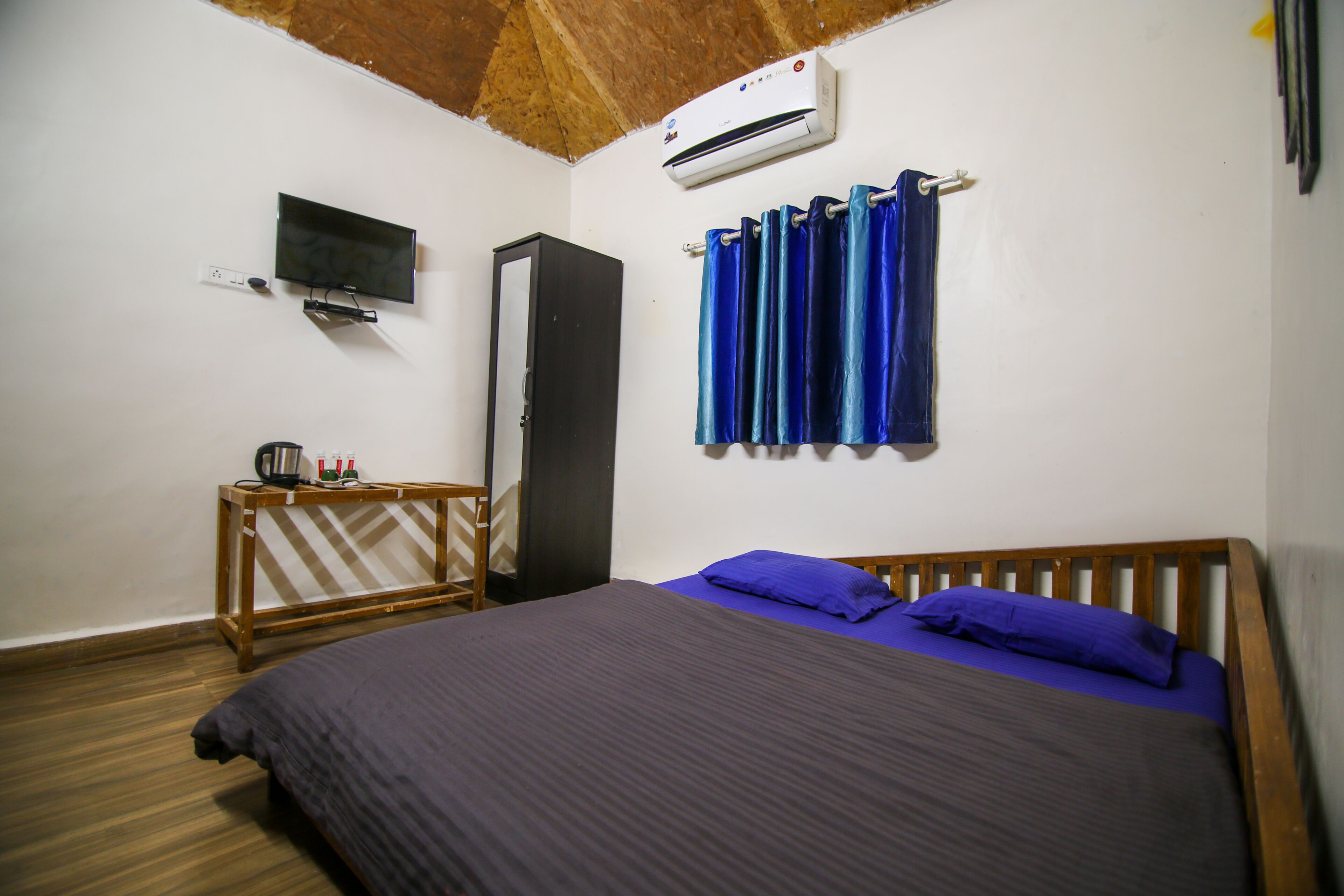 A bedroom with a bed, a TV, an air conditioner, and a wardrobe.