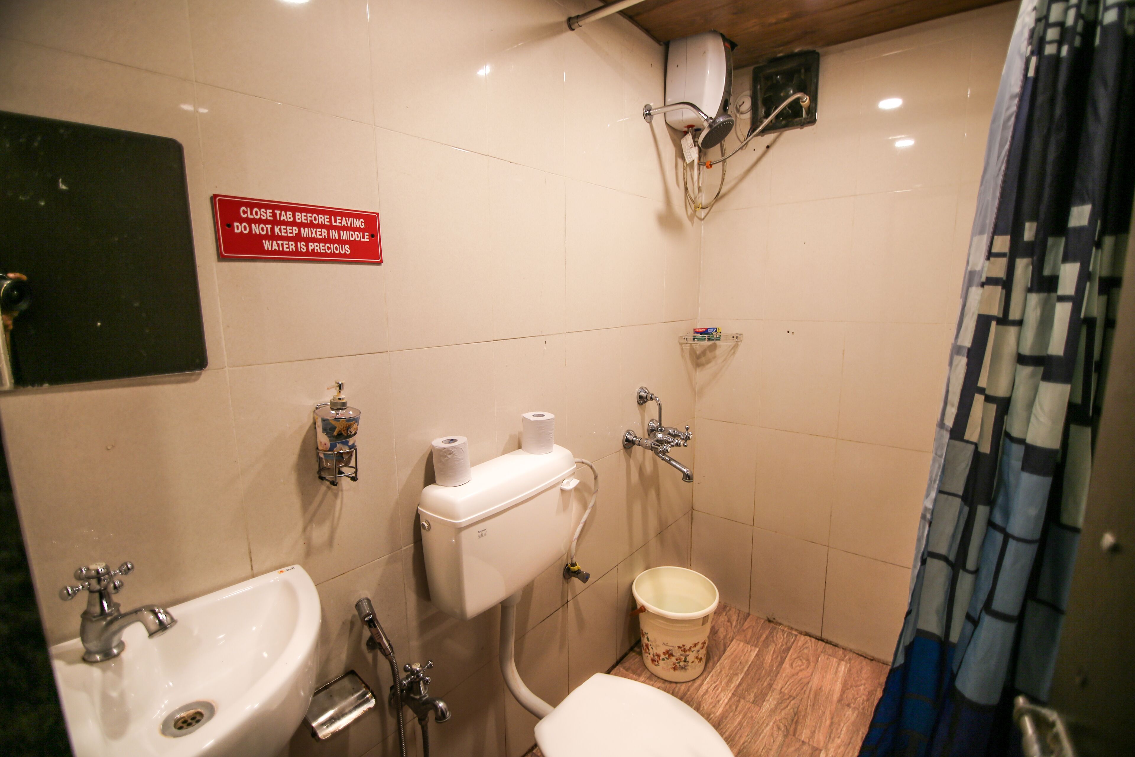 A small bathroom with a sink, toilet, and shower. There is a sign instructing to close the tap before leaving.