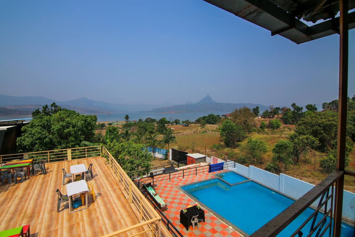 A pool area with a wooden deck, outdoor seating, and a view of the sea and mountains.
