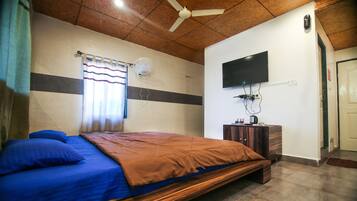 Un dormitorio con cama, ventilador de techo, televisor montado en la pared y ventana con cortinas.