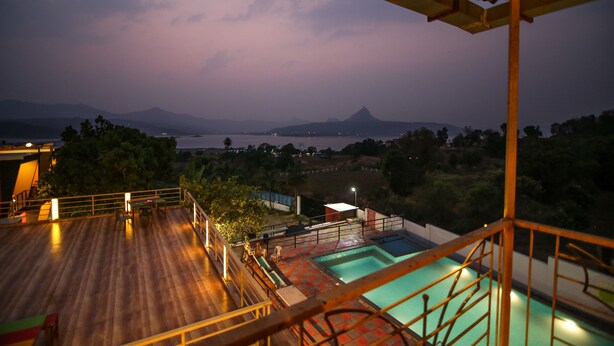 A wooden deck with a pool and a view of a mountain and lake at dusk. - The Bob house (Mawal)
