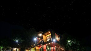 A multi-story building with balconies and large windows, surrounded by trees and a stone wall. - The Bob house (Mawal)