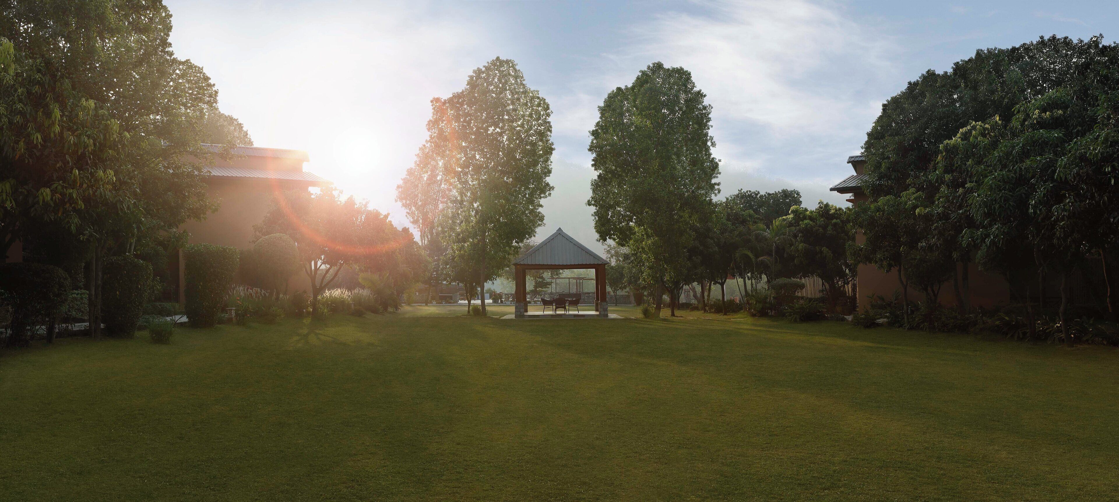 A gazebo in a grassy area with trees and a building in the background.