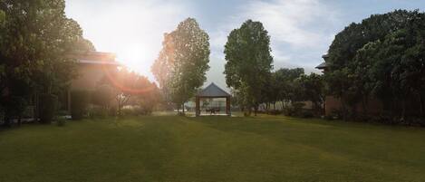 A gazebo in a grassy area with trees and a building in the background.
