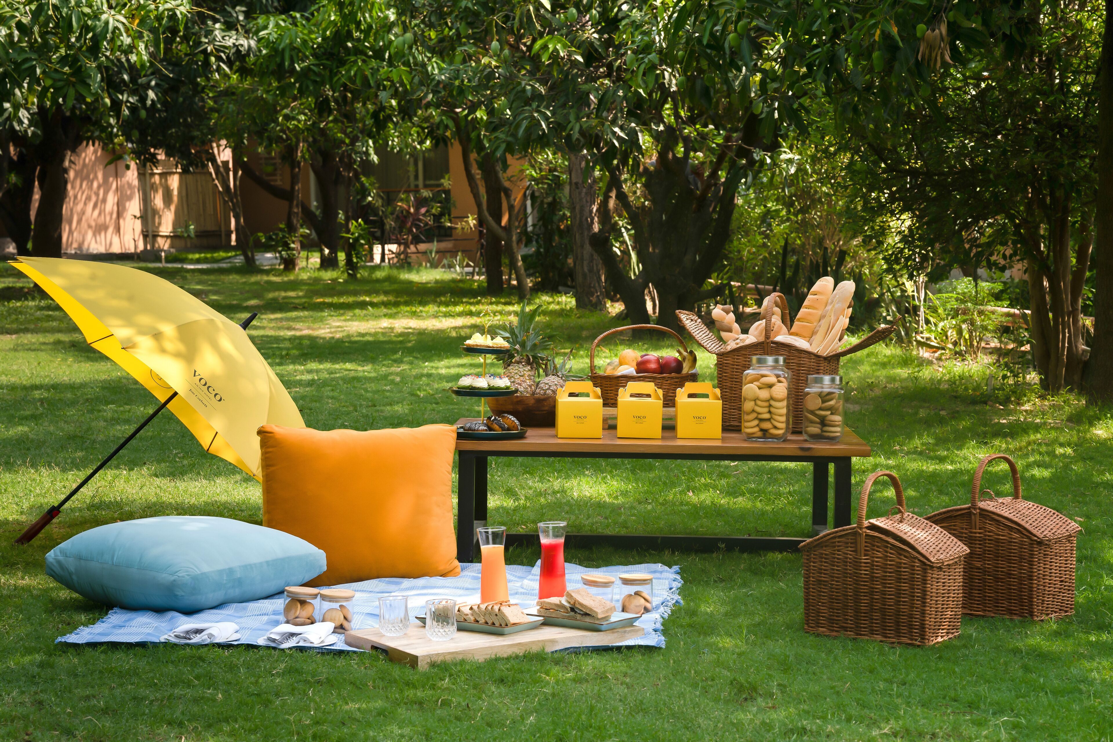 A picnic setup with a table, food, drinks, and baskets in a grassy outdoor area.