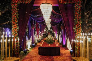 Un espacio interior con un pasillo central, cortinas drapeadas y arreglos florales.