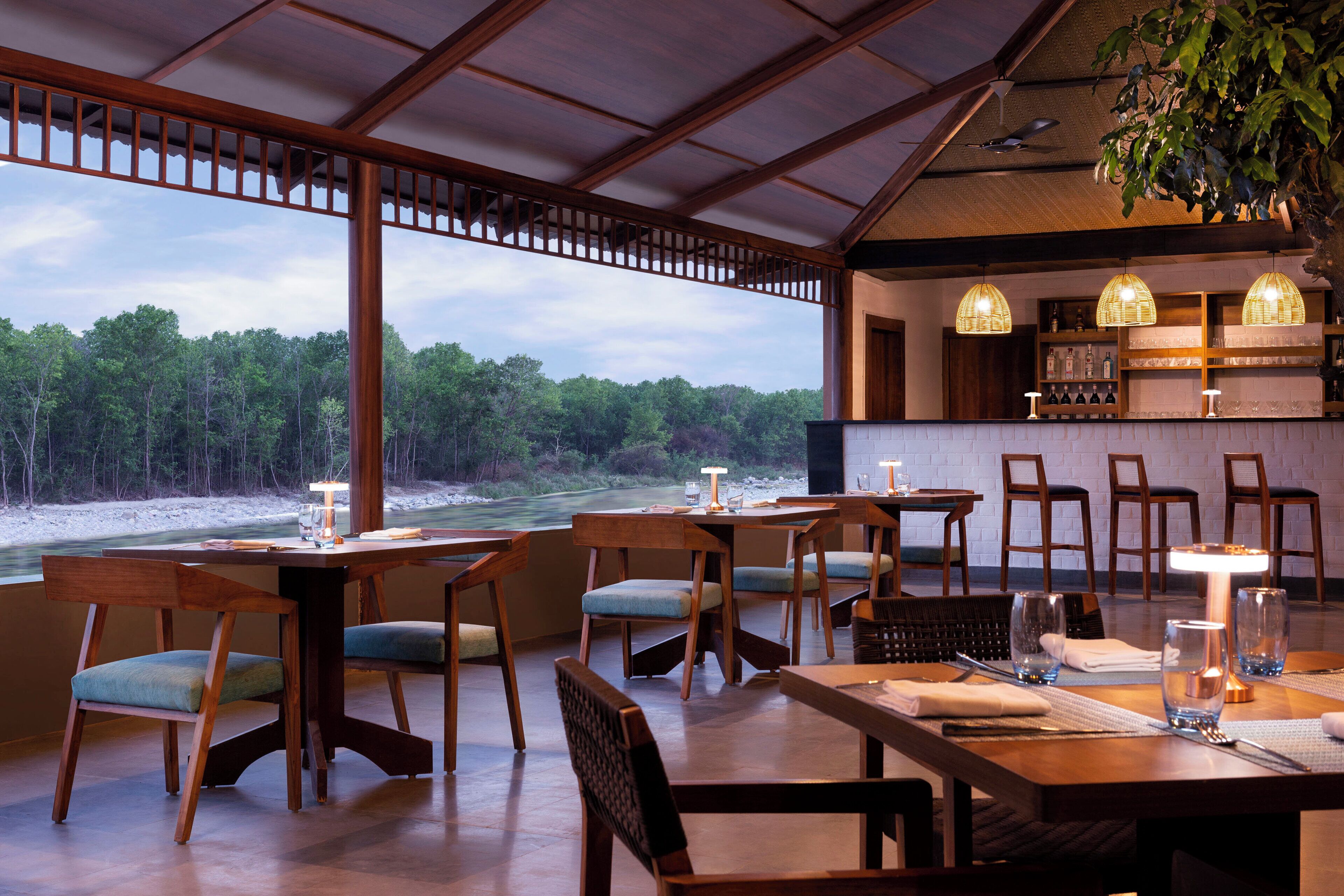 Un restaurante con mobiliario de madera, una zona de bar y vistas a un área boscosa.