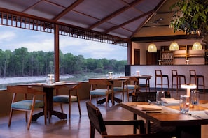 A restaurant with wooden furniture, a bar area, and a view of a forested area. - voco Jim Corbett by IHG (Ramnagar)