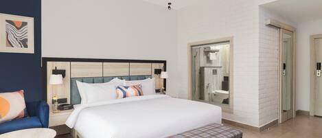 A hotel room with a bed, bedside table, chair, and a bathroom with a shower and toilet.