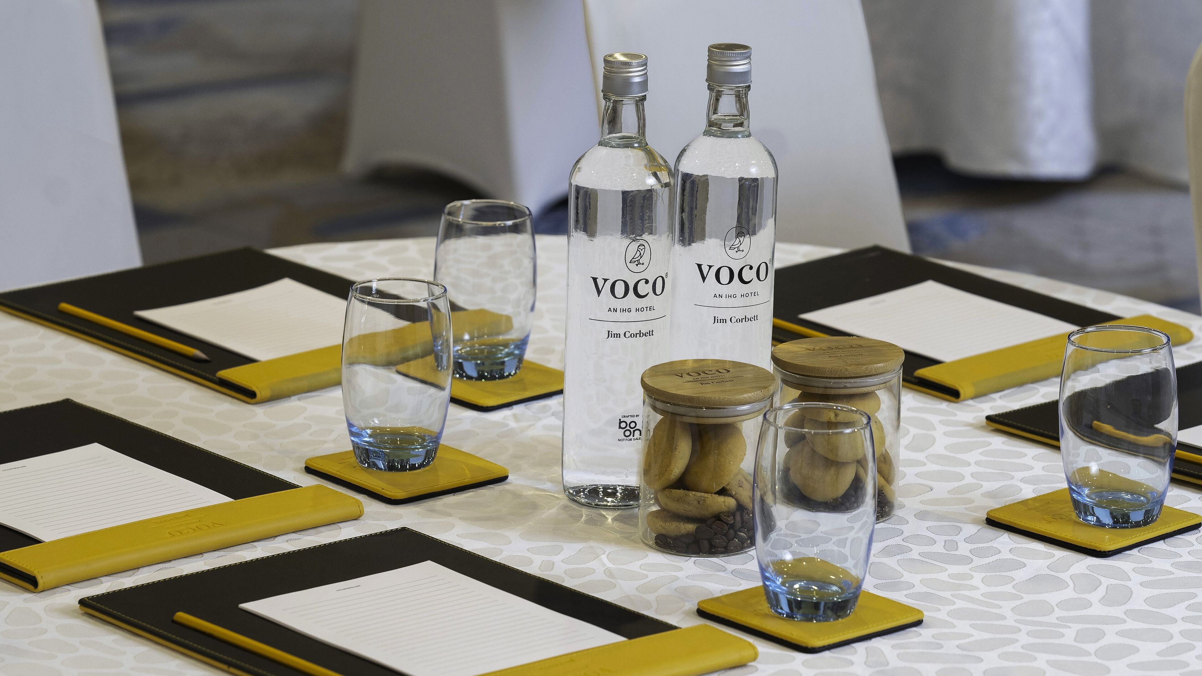 Une table dressée avec de beaux verres, une bouteille de Voco et des pots de noix et de chocolat.
