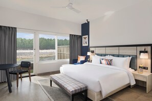 A hotel room with a large bed, a desk, a chair, and a view of the outdoors. - voco Jim Corbett by IHG (Ramnagar)