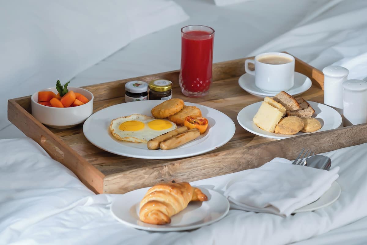 Bandeja de café da manhã com ovos, torradas, croissants e suco sobre a cama.