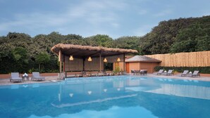 A swimming pool with lounge chairs and a thatched-roof structure. - voco Jim Corbett by IHG (Ramnagar)