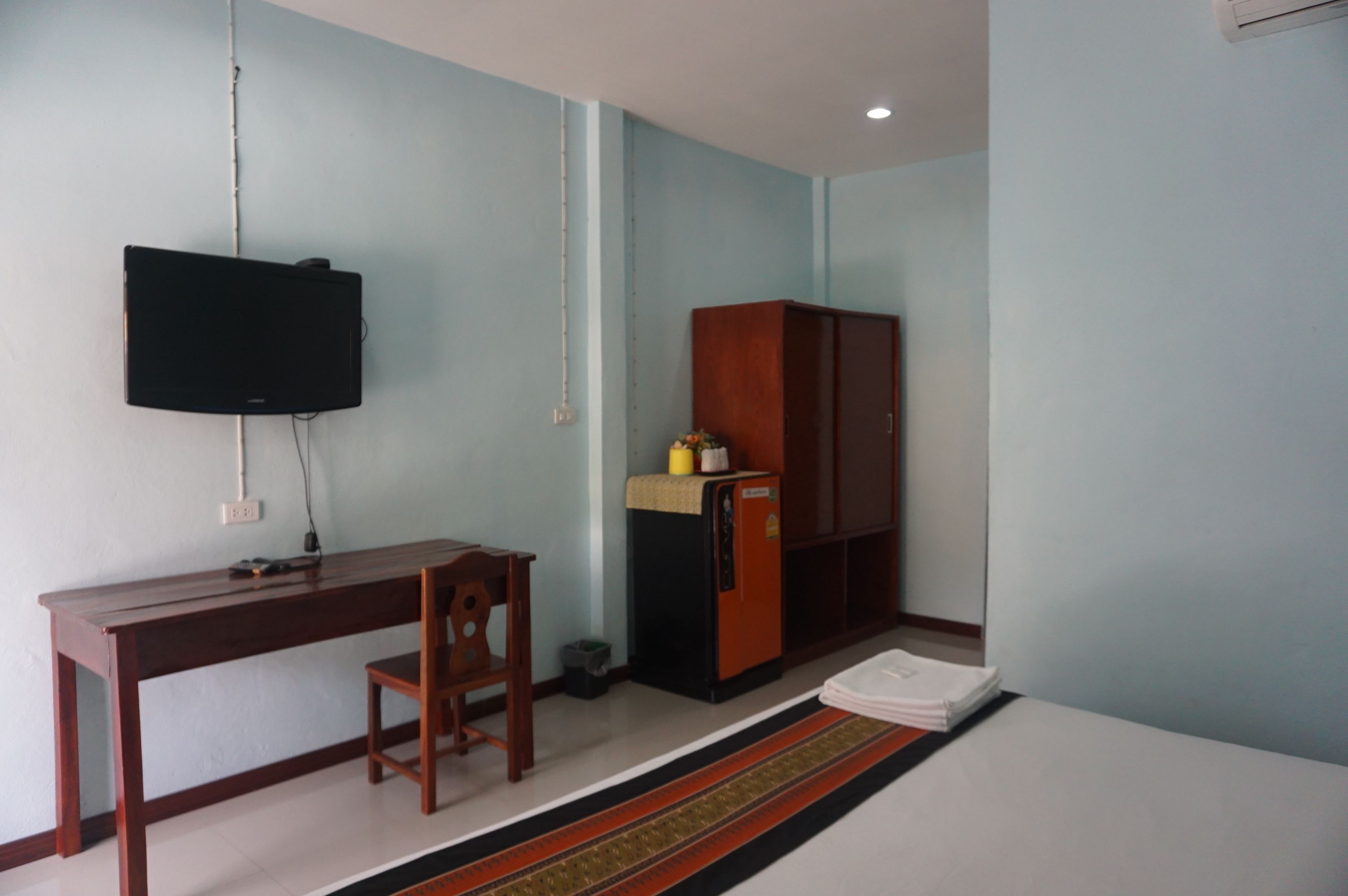 Una habitación con escritorio, silla, televisor, armario y un refrigerador pequeño.
