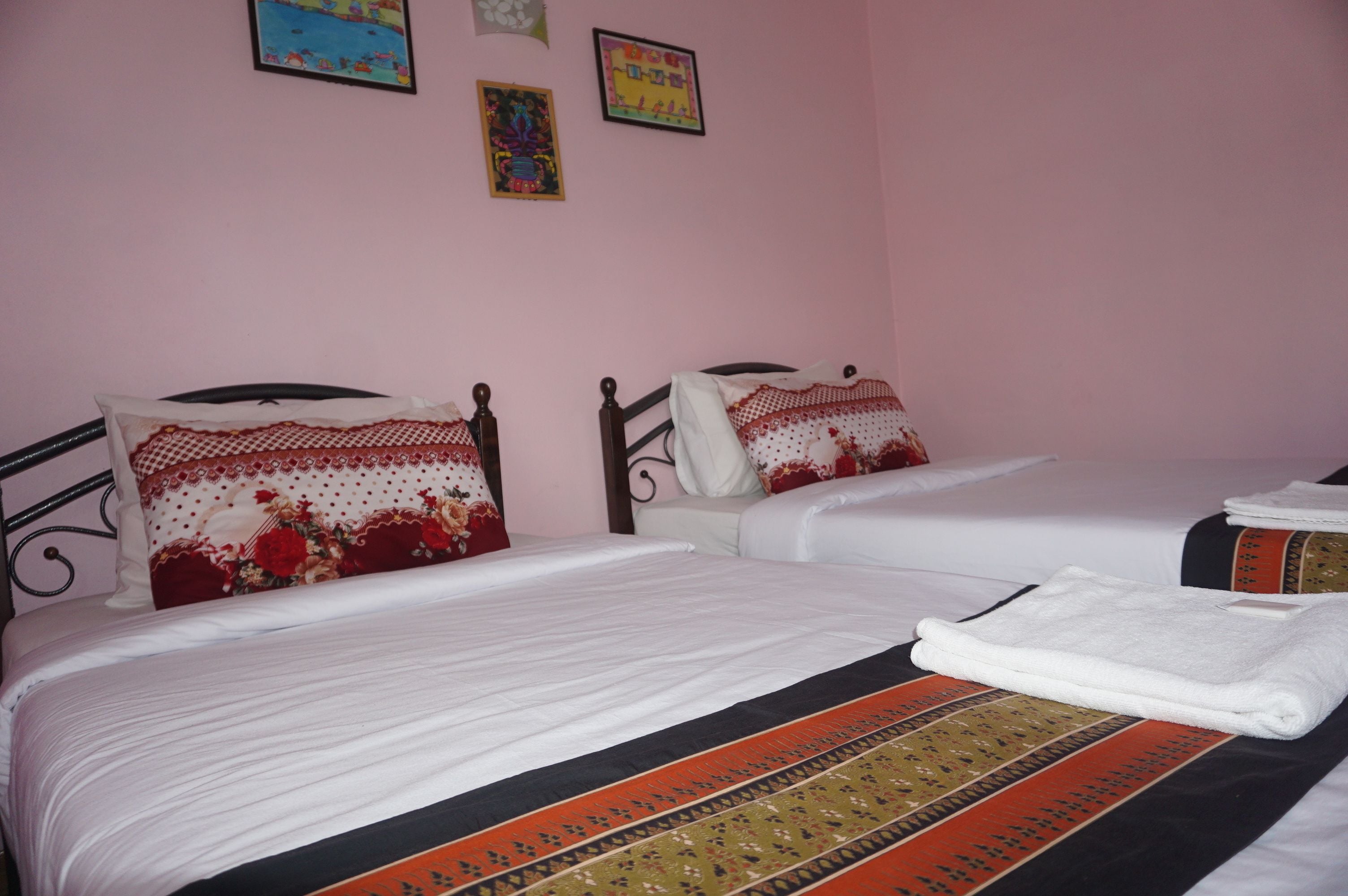 Habitación de hotel con dos camas, cada una con cubrecama blanco y almohadones decorativos. Hay cuadros enmarcados en la pared y una toalla blanca doblada sobre la cama.