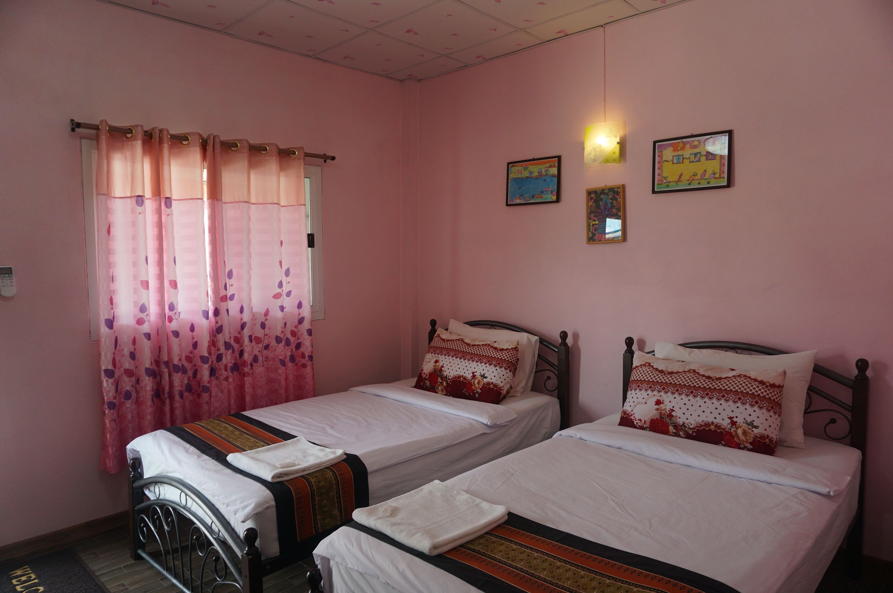 Une chambre avec deux lits simples, des murs roses et une fenêtre ornée de rideaux à motifs floraux roses.