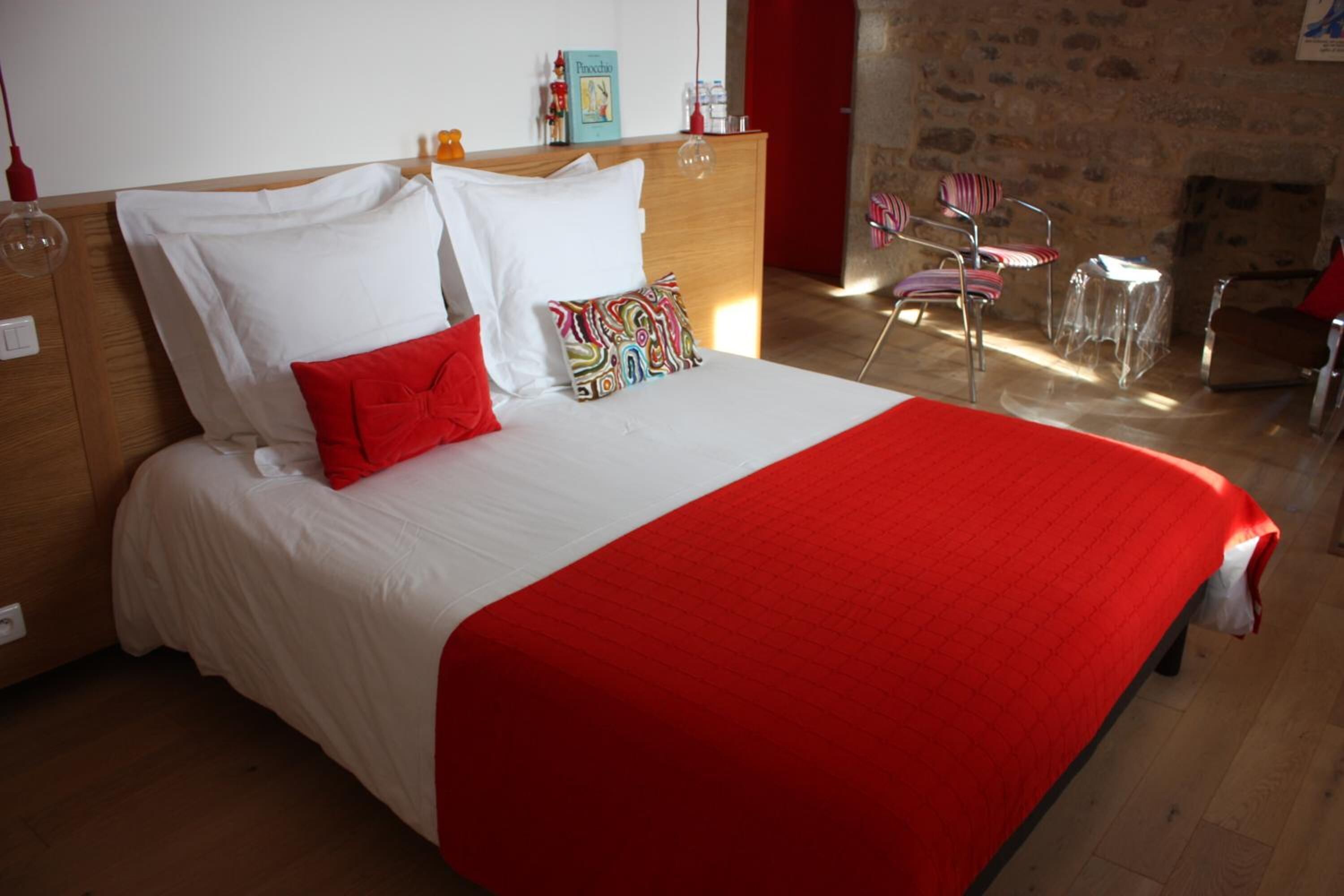 Un lit avec une literie blanche et rouge, une tête de lit en bois et un coussin coloré.
