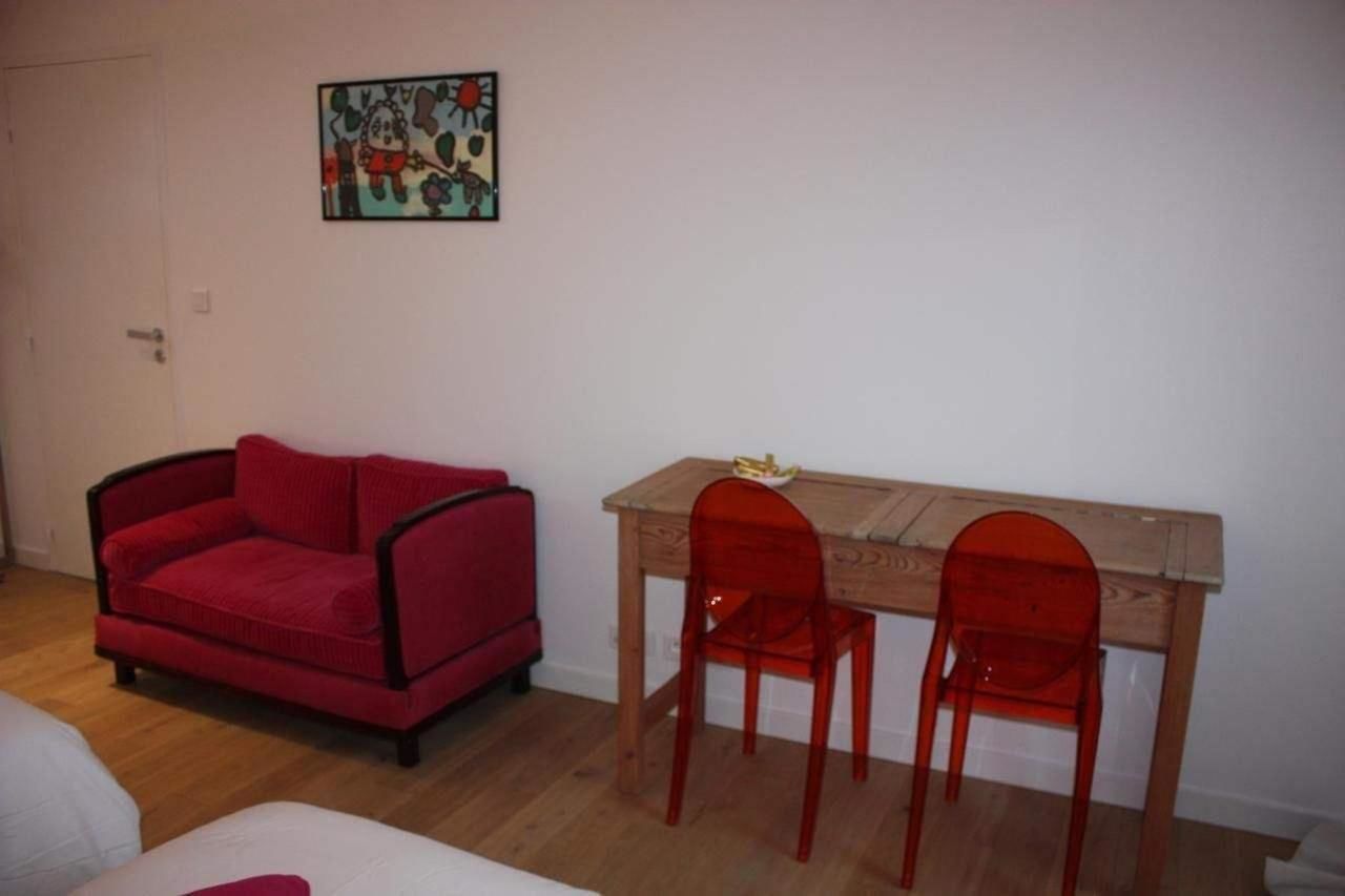 A room with a red sofa, a wooden table with two red chairs, and a wall-mounted picture.
