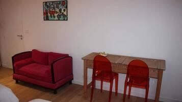 A room with a red sofa, a wooden table with two red chairs, and a wall-mounted picture.