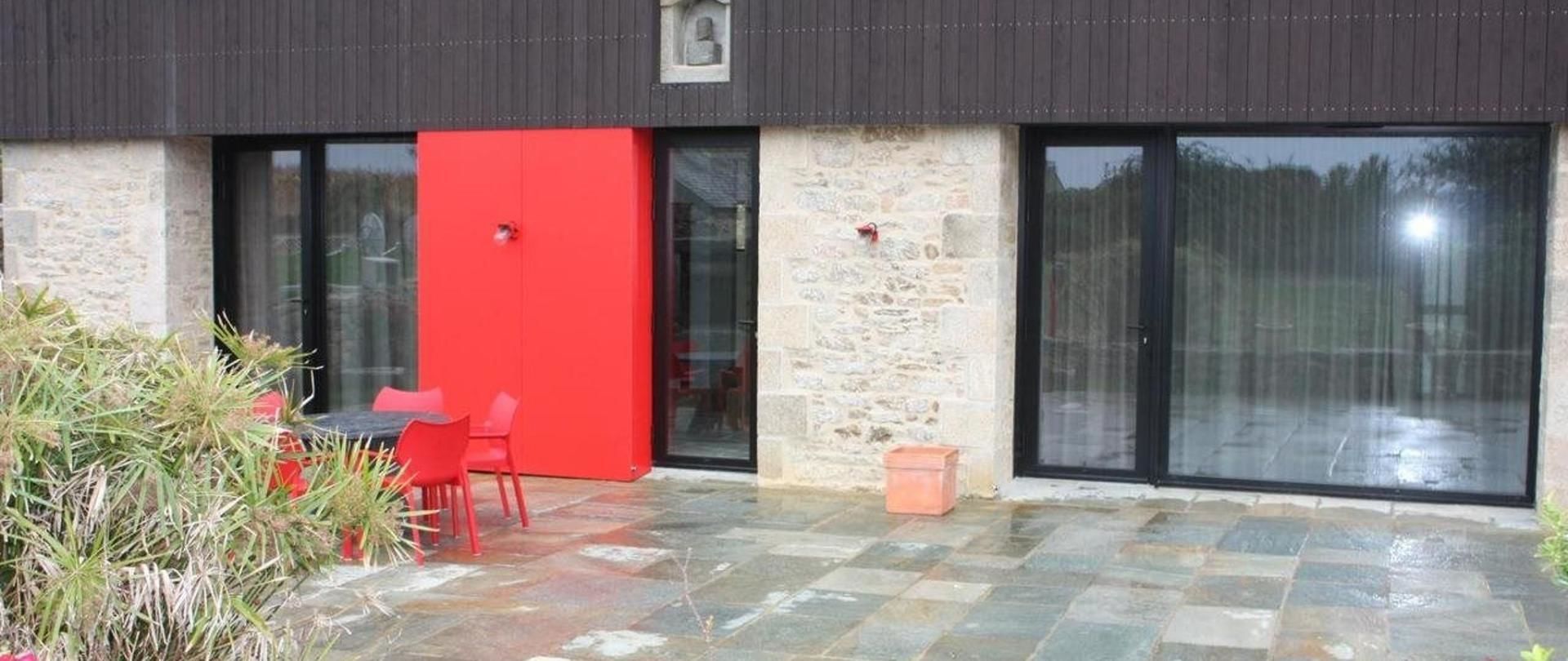 A modern building with a stone facade, large windows, and a red door.